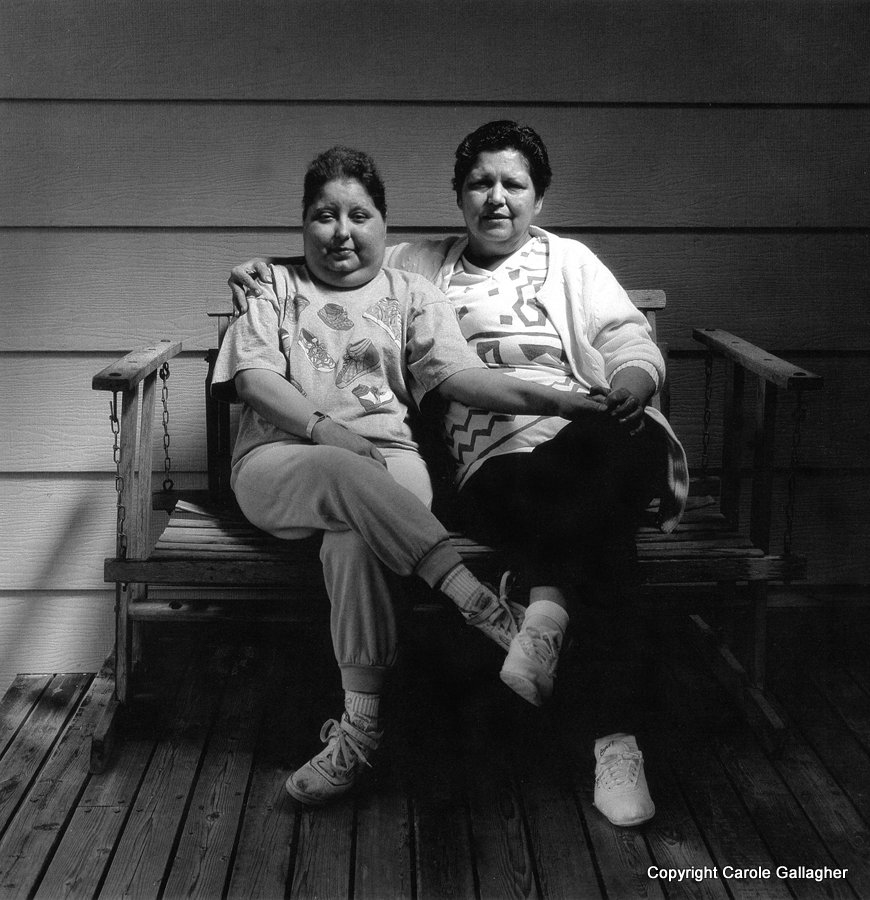 A woman sits with her daughter on a bench on a porch.