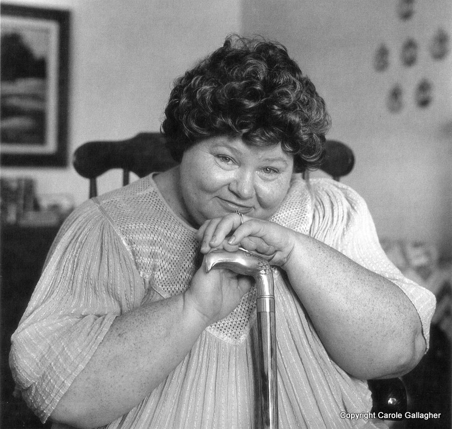 A woman with short curly hair leans on a cane with an eagle head handle.