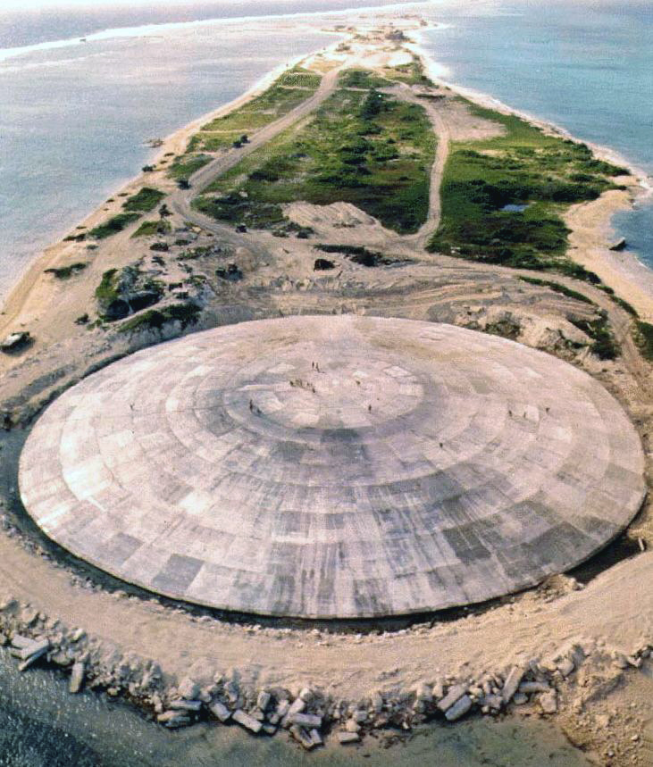 A giant cement dome dominates a small atoll. Small specks of people can be seen walking across the dome; the island stretches into the background.