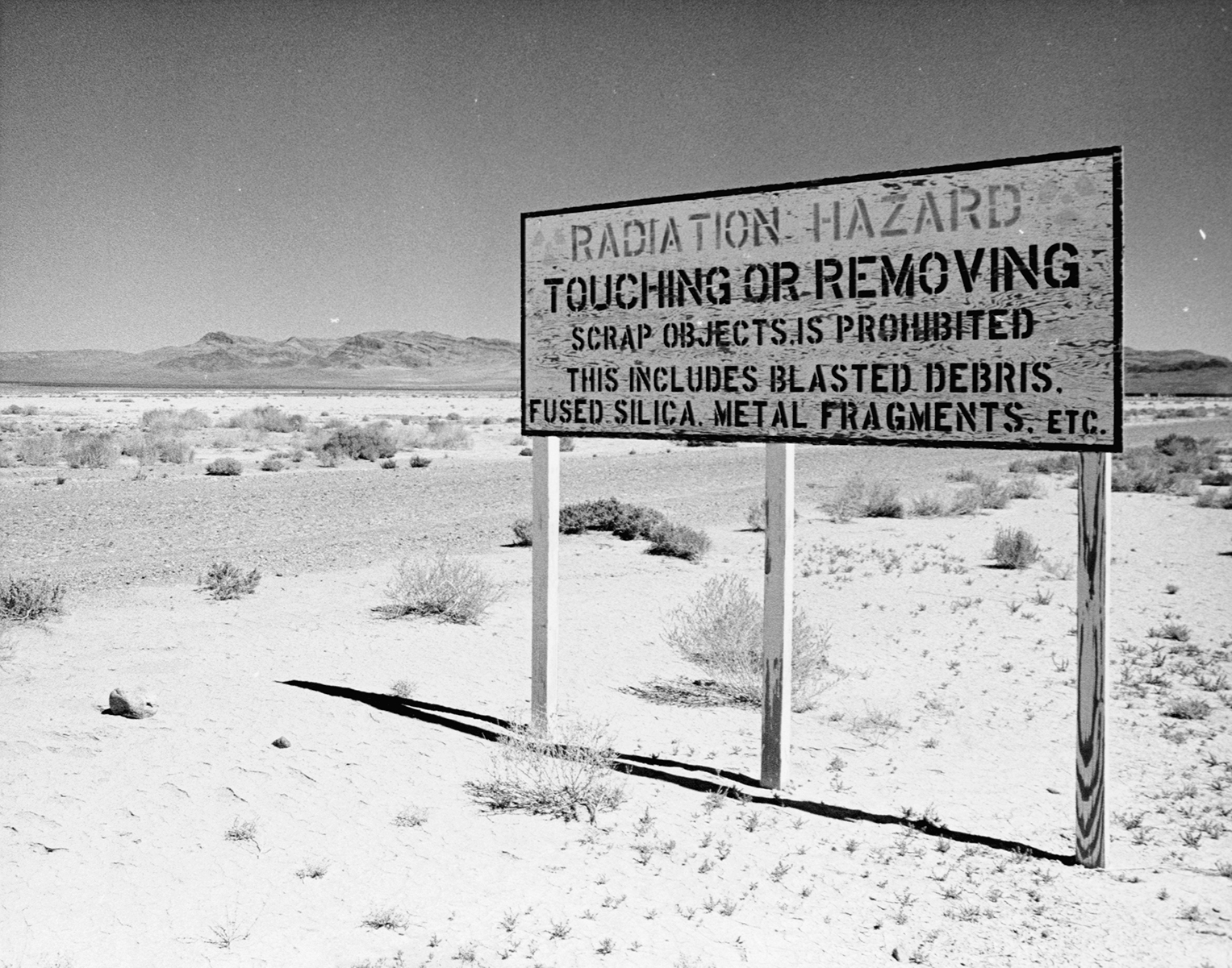 A sign in a desert reads, 'Radiation Hazard: Touching or removing scrap objects is prohibited: This includes blasted debris, fused silica, metal fragments, etc.'