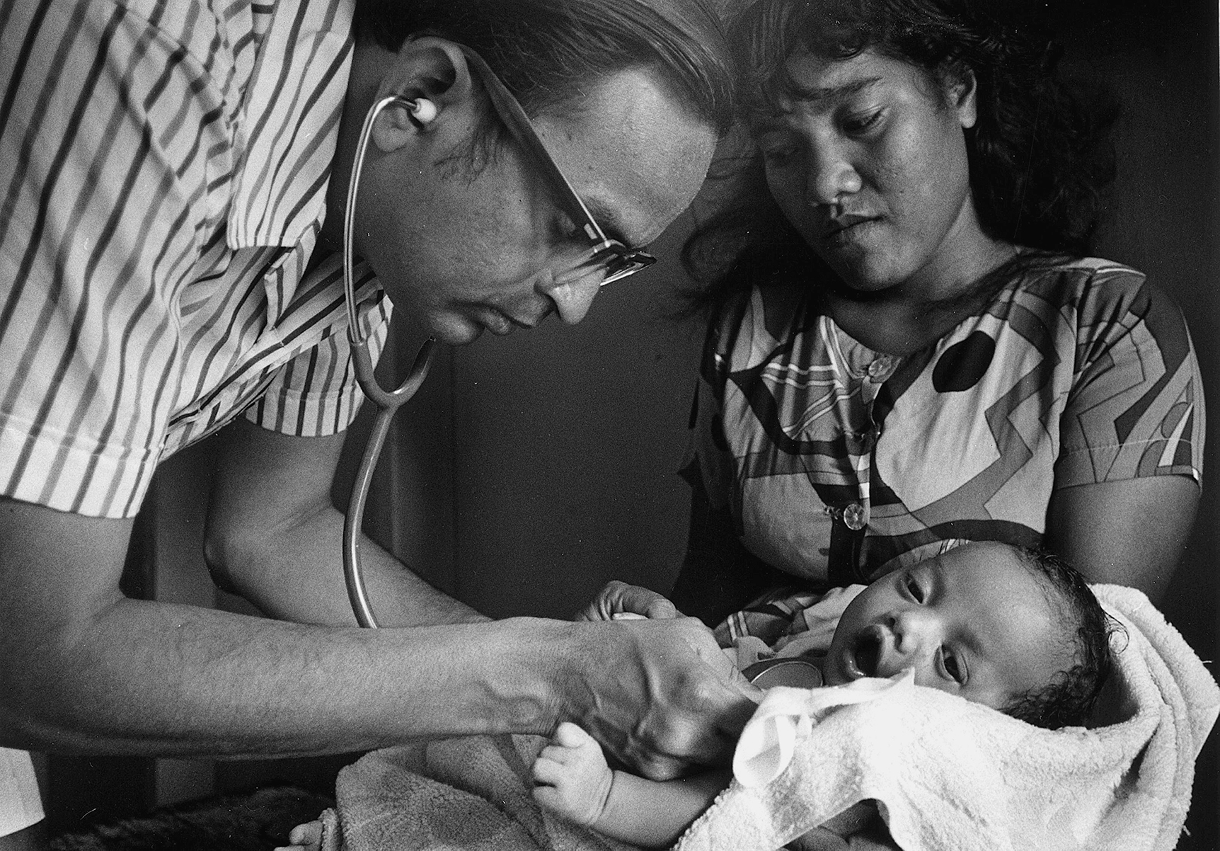 A doctor listens to the heartbeat of an infant, in the presence of a concerned mother.