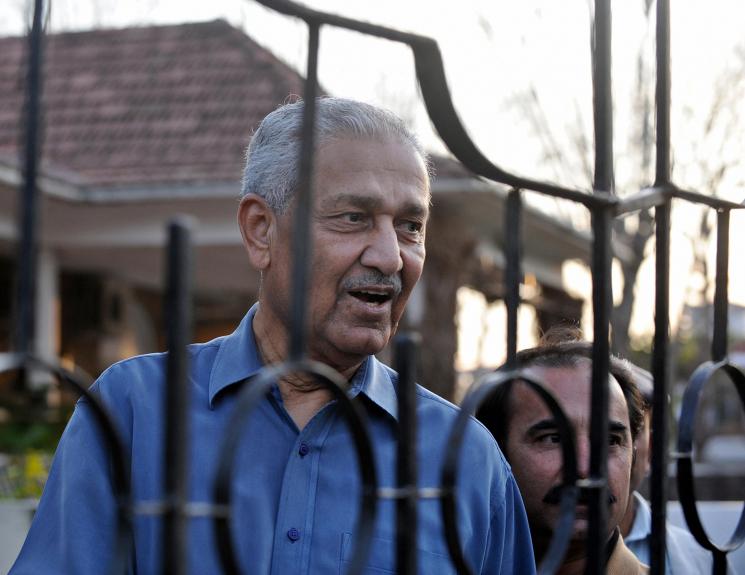 An older man is visible beyond a gate, he appears to be speaking to someone out of frame.