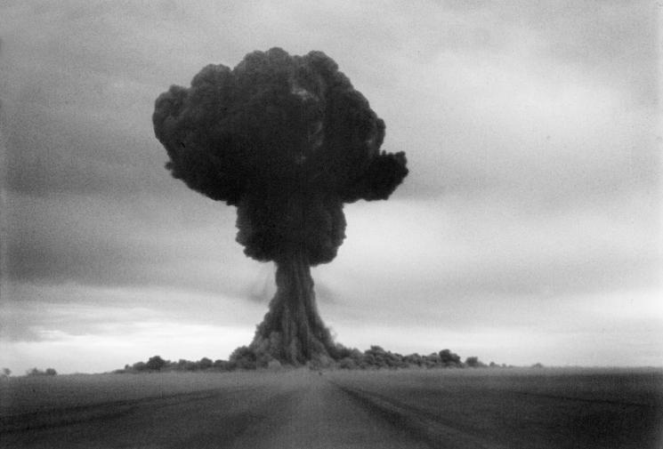 A large black mushroom cloud is visible against a light-grey clouded sky.