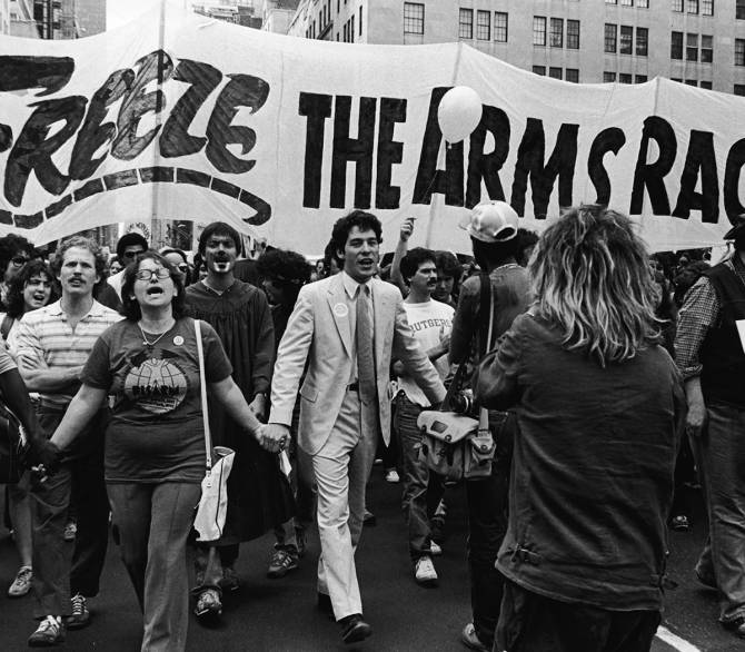A man in a suit leads a protesting crowd holding a banner that reads, 'Freeze the arms race'.