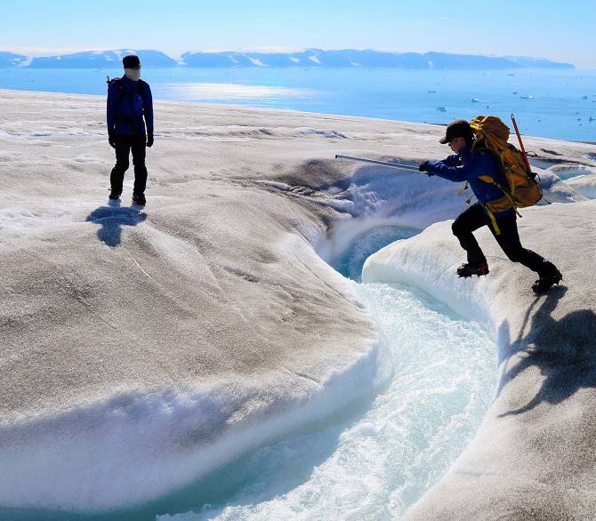 Scientists cross a river on a glacier