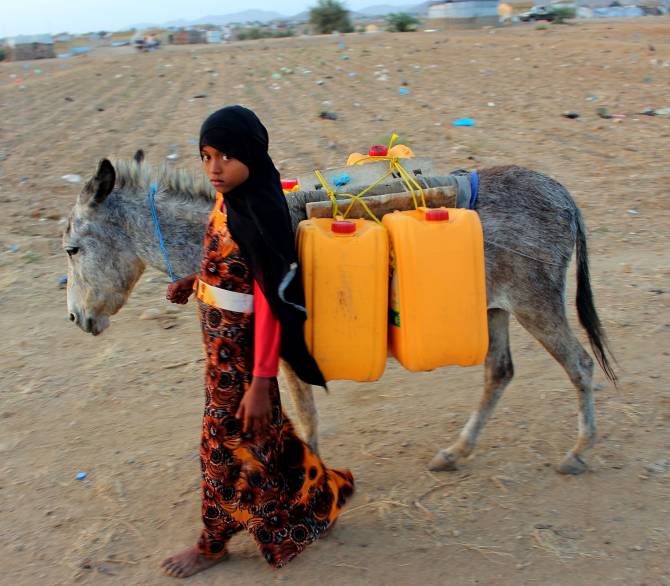 A girl walks with a donkey carrying jerry cans filled with water from a cistern at a make-shift camp for displaced Yemenis in severe shortage of water, in the northern Hajjah province on March 24, 2020; Getty