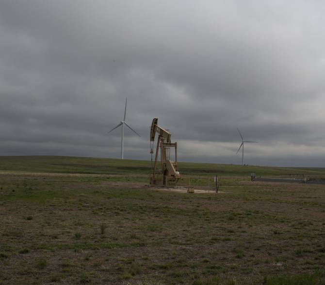 A natural gas pump sits on land next to wind mills, as fracking and wind power are both common sights along the roads, May 10, 2021, in rural Western Oklahoma. 
