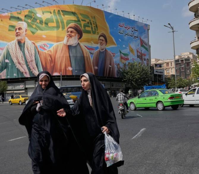Two women walk past a huge banner showing the late commander of the Iran's Revolutionary Guard expeditionary Quds Force, Gen. Qassem Soleimani, who was killed in a U.S. drone attack in 2020, and two late Hezbollah leaders Hassan Nasrallah, center, and Hasem Safieddine, who were killed in Israel airstrikes in 2024, at the Enqelab-e-Eslami (Islamic Revolution) square, in Tehran, Iran, Saturday, Sept. 27, 2025.