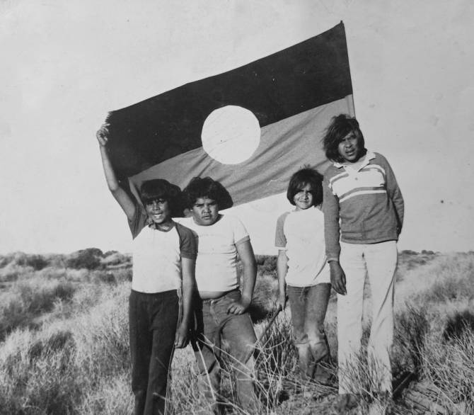 Kokatha Country, and thus Kokatha culture, came under considerable threat from uranium mining in the 1980s. Recognizing the power of Kokatha knowledge of, and connection to, Country, Kokatha boys Stanley Wingfield, Sydney Amos, Glen Wingfield, and Terry Strangeway hold an Aboriginal flag on their Country near Olympic Dam, circa 1983. Photograph courtesy of the Wingfield family.