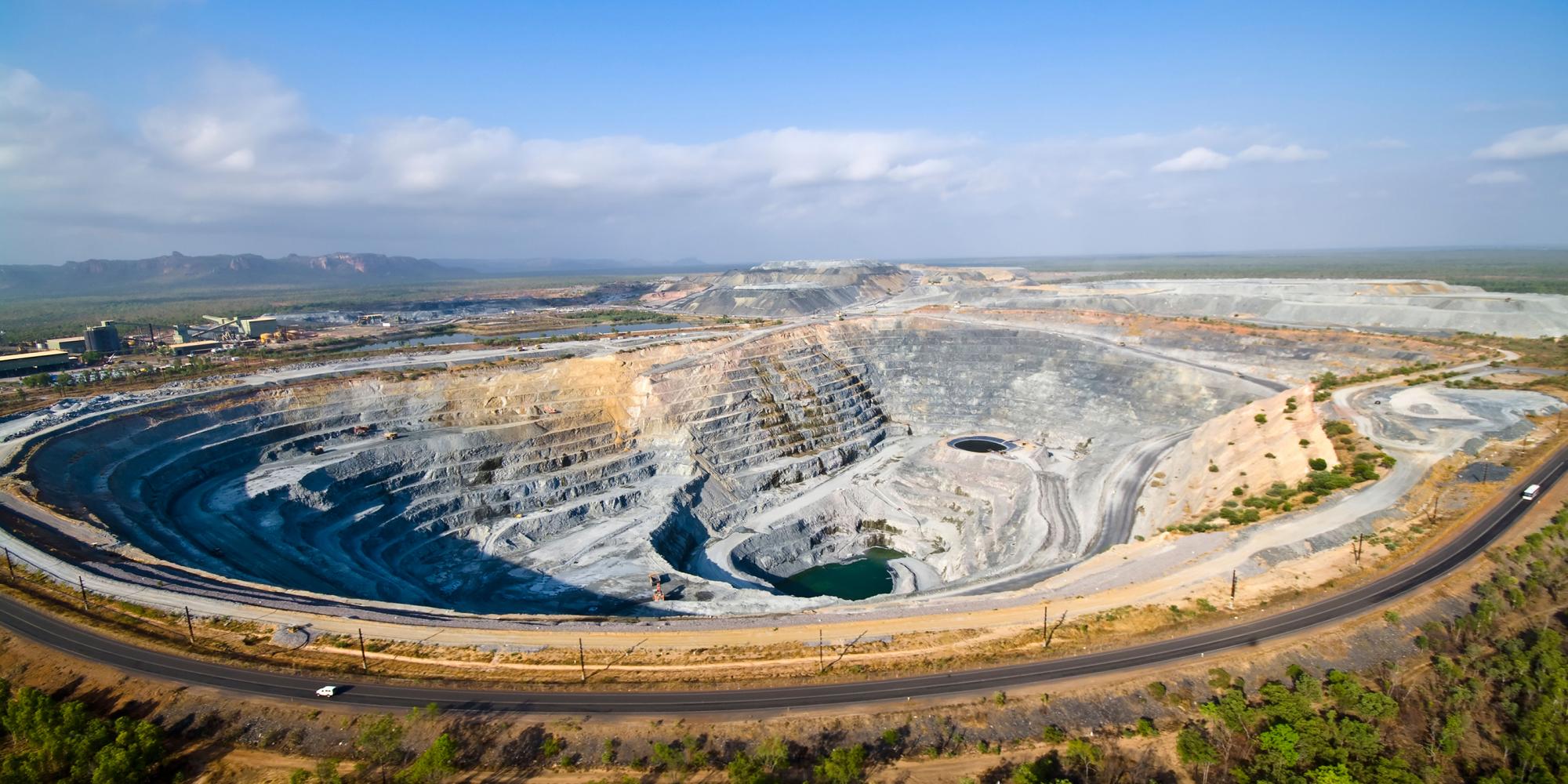 A large grey strip mine, with a stepped decline to the bottom, disrupts a green plains landscape.